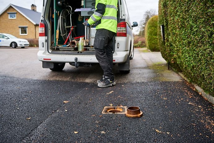 En förbindelsepunkt i en gata i förgrunden, intill en villatomt. I bakgrunden syns en skåpbil och en person i varselkläder.